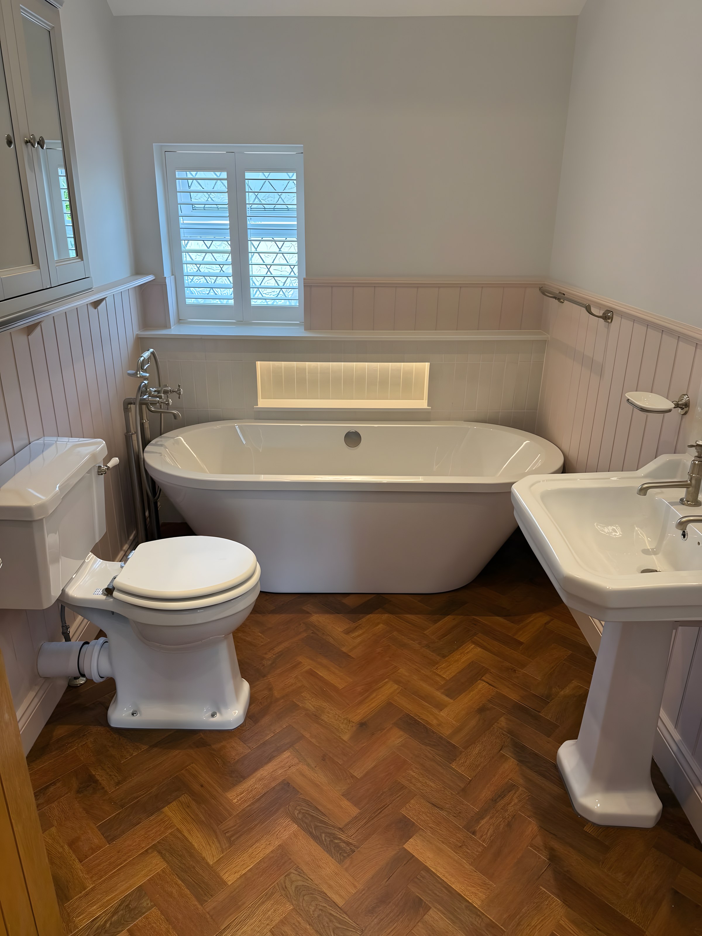Pale pink panelled bathroom with freestanding bath and herringbone floor
